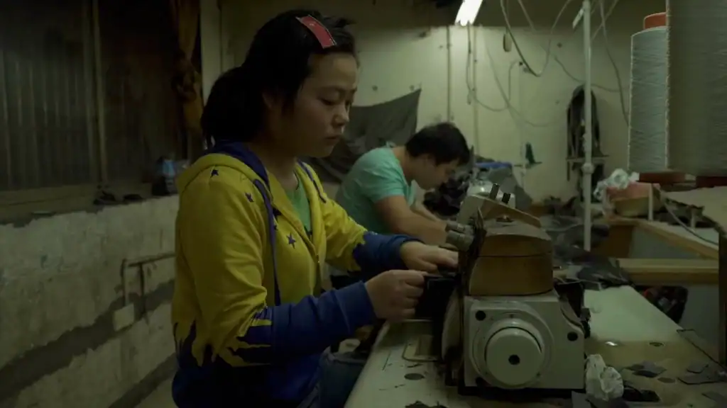 Woman sewing in dimly lit factory, Zhili town, from Wang Bing’s Youth (Homecoming).