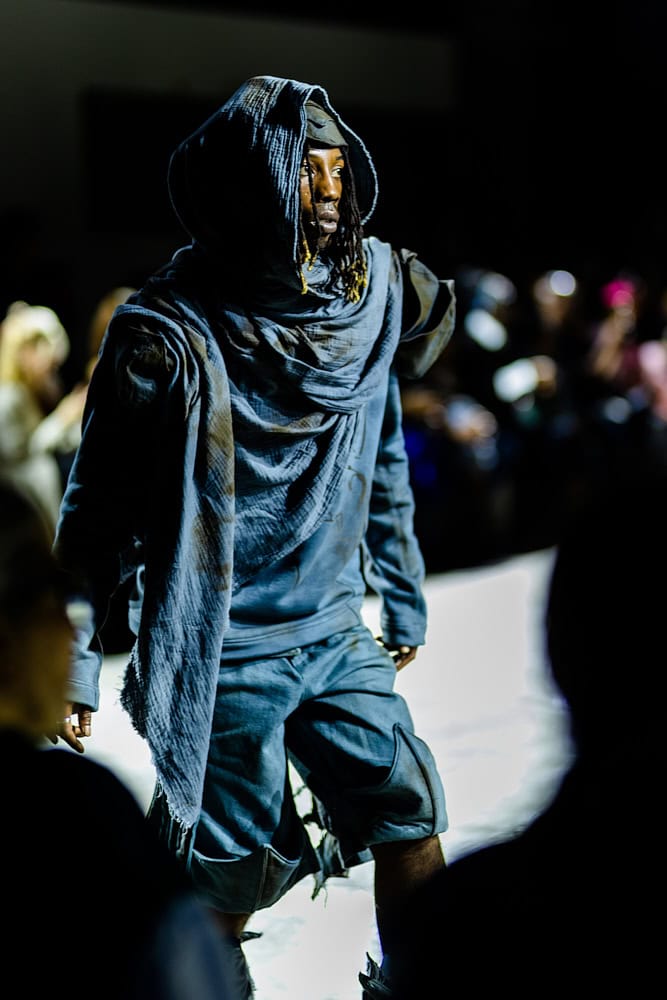 Model in dark indigo hooded outfit and sculptural layers, photographed by Hannah Khatib for Yaku Stapleton’s “A Ground to Stand On.”