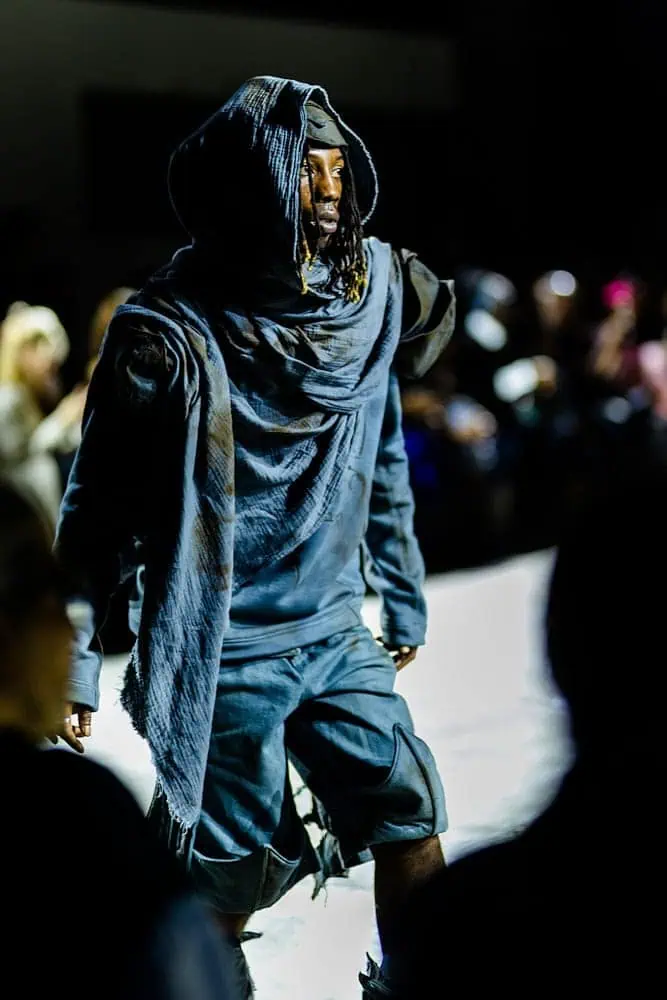 Model in dark indigo hooded outfit and sculptural layers, photographed by Hannah Khatib for Yaku Stapleton’s “A Ground to Stand On.”