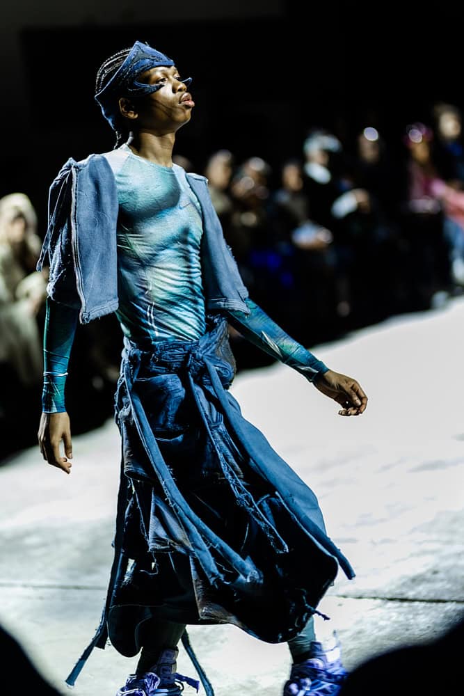 Model in blue deconstructed outfit and headpiece walking the runway, photographed by Hannah Khatib for Yaku Stapleton’s “A Ground to Stand On.”