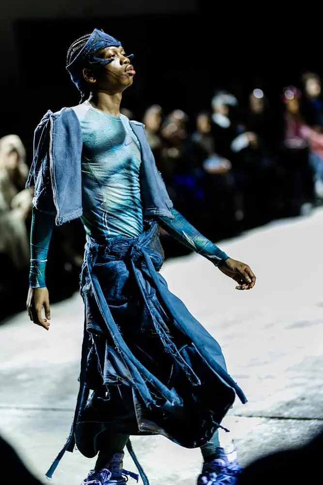 Model in blue deconstructed outfit and headpiece walking the runway, photographed by Hannah Khatib for Yaku Stapleton’s “A Ground to Stand On.”