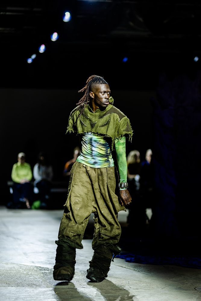 Model wearing distressed green ensemble with asymmetrical textures at Yaku Stapleton’s “A Ground to Stand On,” captured by Hannah Khatib.