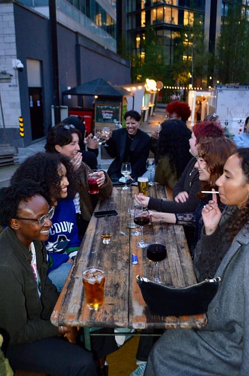 Group of friends laughing and sharing drinks at the Sapphic Cinema queer community event.
