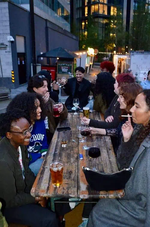 Group of friends laughing and sharing drinks at the Sapphic Cinema queer community event.