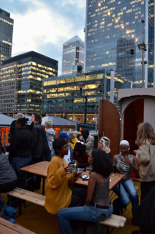 Attendees socialising on the boat deck at Sapphic Cinema with the Canary Wharf skyline at dusk.