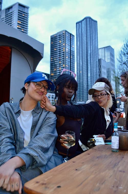 Three friends enjoying drinks and posing together at the Sapphic Cinema boat event in Canary Wharf.
