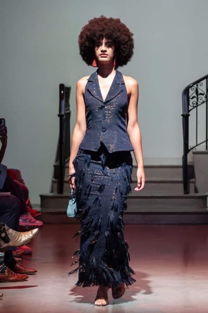 A woman wearing a blue dress and red earrings showcases the creativity of emerging designers.