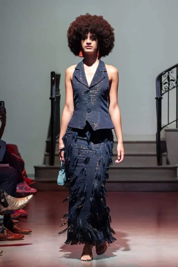 A woman wearing a blue dress and red earrings showcases the creativity of emerging designers.
