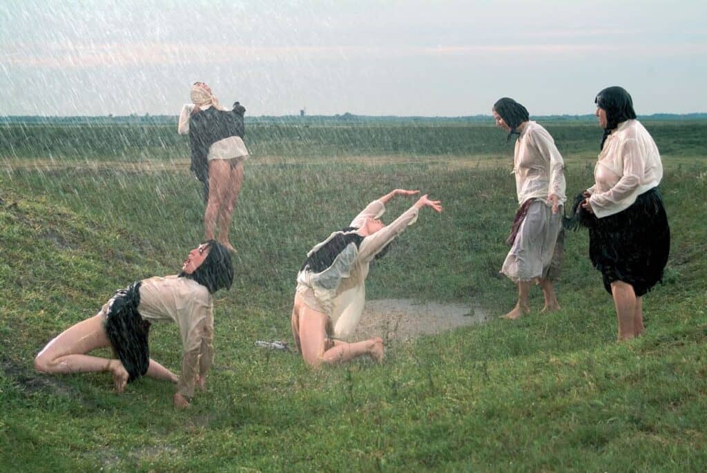 Performers interacting physically with grass in an open field during Balkan Erotic Epic, emphasizing the body’s connection to nature and desire.