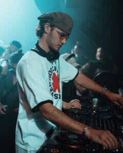 Close-up of Mau P focused on mixing during a DJ set, wearing headphones and a white t-shirt, captured in Ibiza for Cold Magazine feature on his rise to fame.
