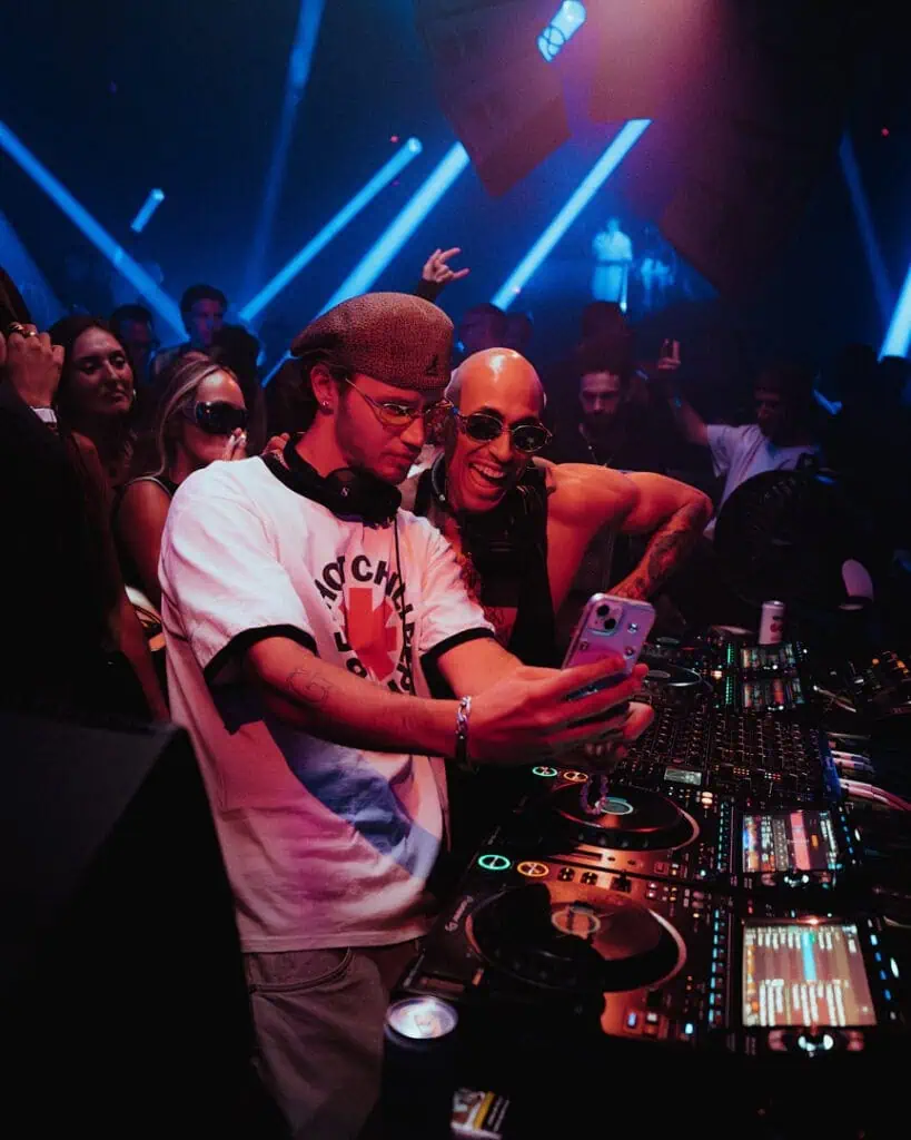Mau P DJing alongside another artist in a crowded club with blue neon lights, photograph courtesy of the artist for Cold Magazine interview on stardom and his new track “Tesla”.