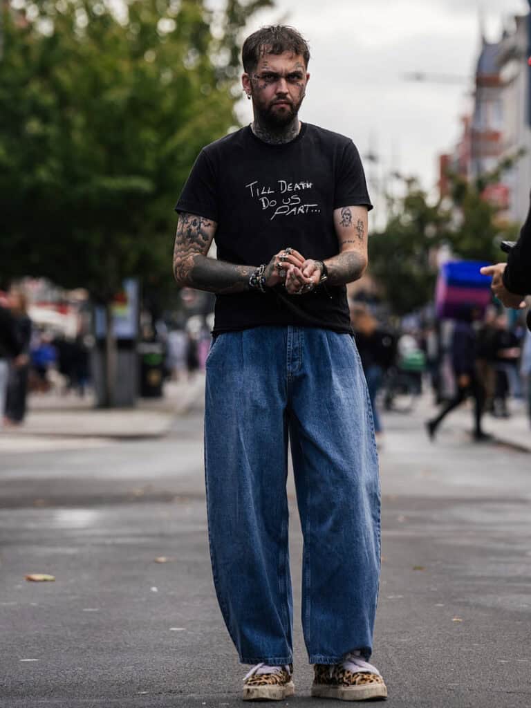 Mason Newman standing in the street wearing a black graphic tee and oversized blue jeans from the Romance at the Rodeo collection.
