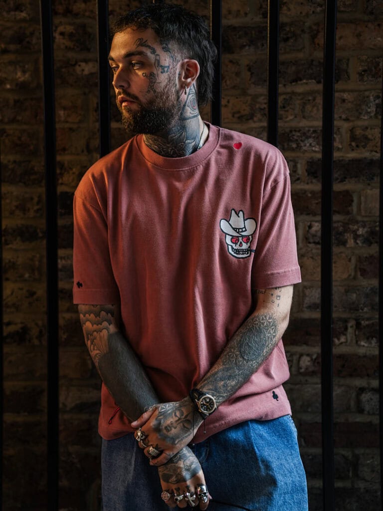 Close-up of Mason Newman in a pink graphic T-shirt, showing his signature tattoos and jewellery from his Topman collaboration.