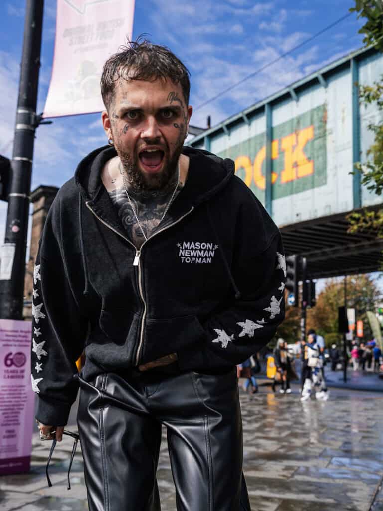 Mason Newman shouting playfully under a bridge in Camden, wearing a black Mason Newman x Topman hoodie and leather trousers.