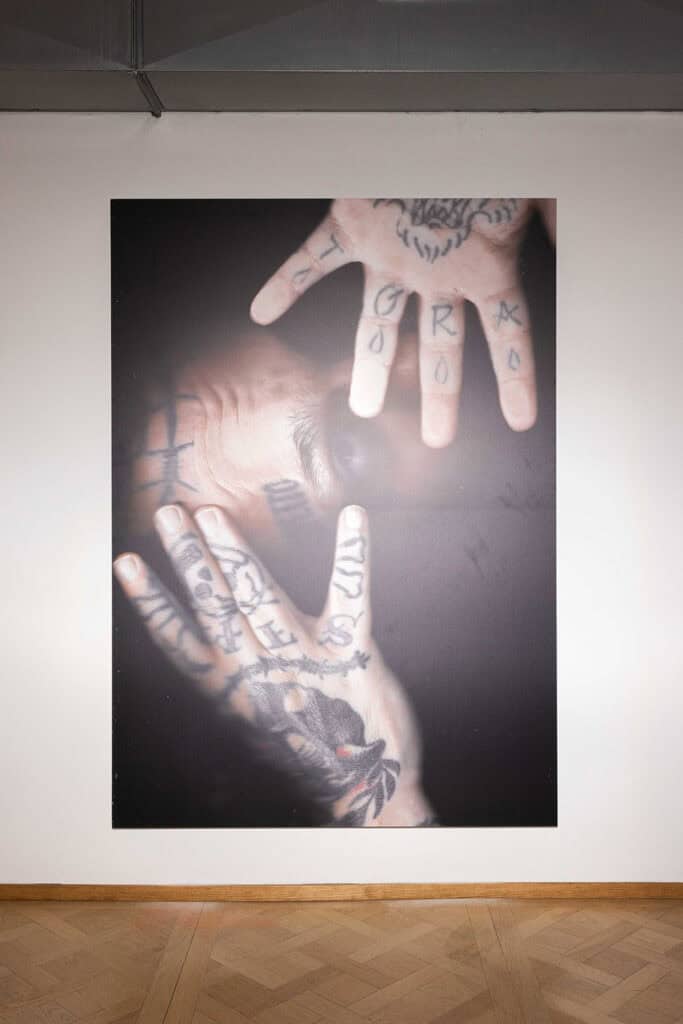 Close-up photographic print of tattooed hands overlapping and touching, shown in Cate Colapietro’s “Breath Not Found” exhibition.