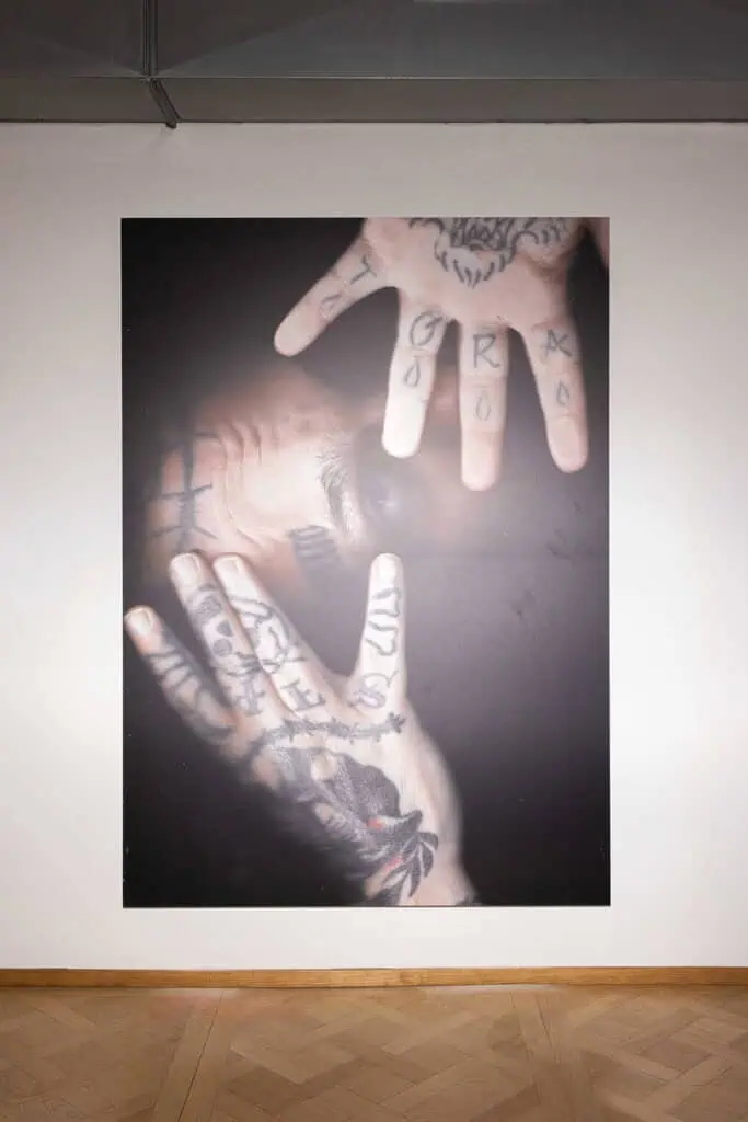 Close-up photographic print of tattooed hands overlapping and touching, shown in Cate Colapietro’s “Breath Not Found” exhibition.