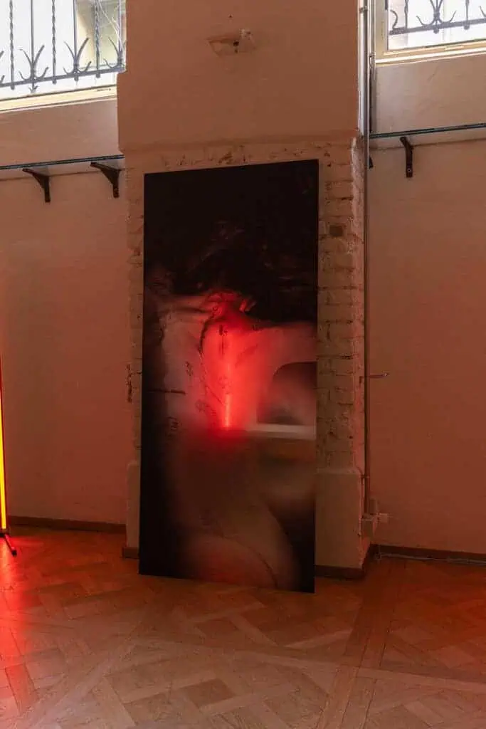 Large-scale photograph with red-tinted lighting displayed in a dim gallery space as part of Cate Colapietro’s “Breath Not Found” exhibition.