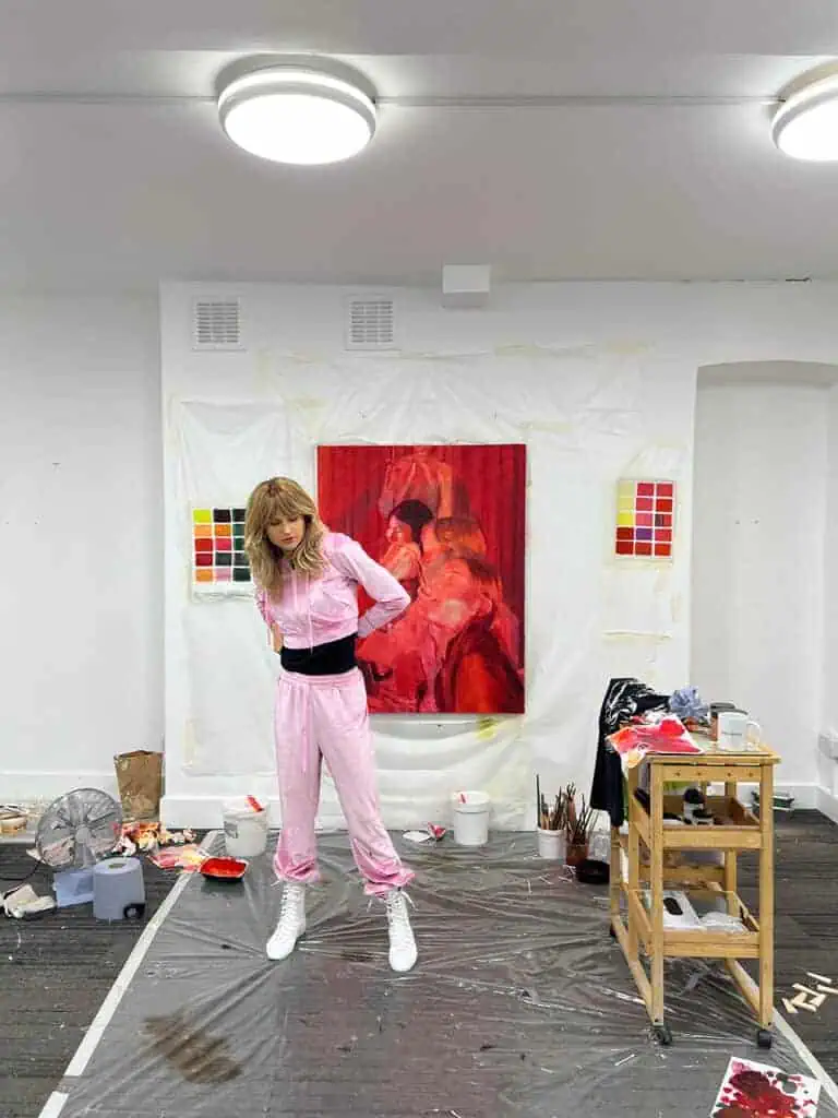 Artist studio scene from Nana Wolke’s “Nothing Left to Want” project, showing Nana in front of a large red painting surrounded by paints and materials.