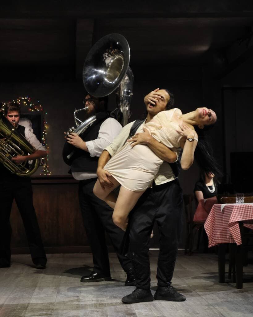 Scene from Balkan Erotic Epic where a performer is lifted in a ceremonial gesture while a live brass band plays in the background.