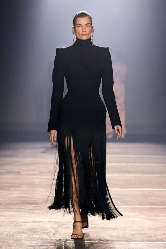 Mugler SS26 long black gown with sharp structured shoulders and fringe hem movement.