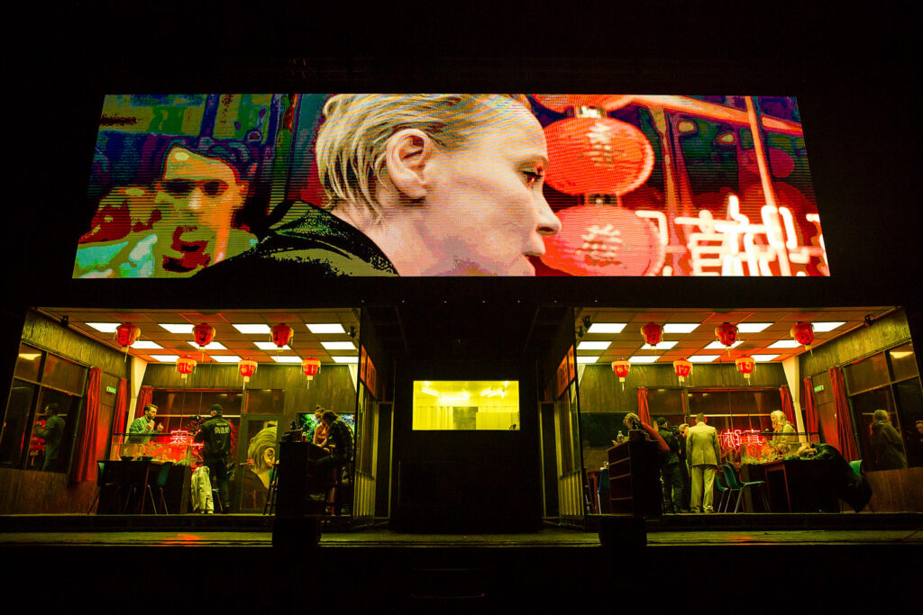 Exterior view of a neon-lit Chinese restaurant with cinematic red lighting, still from Łukasz Twarkowski’s “ROHTKO”, photographed by Artūrs Pavlovs for Cold Magazine feature on authenticity and AI in art.