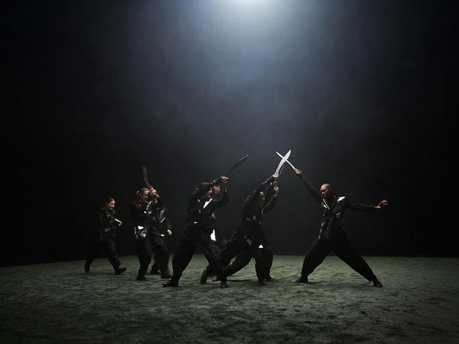 Performance from Marina Abramović’s Balkan Erotic Epic, with a group of performers moving in ritual formation under a theatrical spotlight.