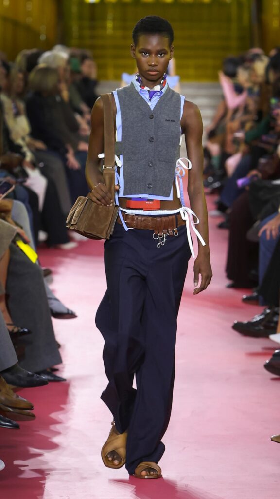 Miu Miu SS26 grey sleeveless vest styled with navy trousers and layered belt.