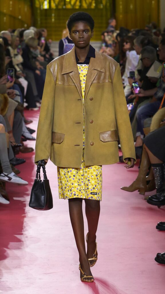 Miu Miu SS26 oversized tan jacket styled over yellow printed dress.