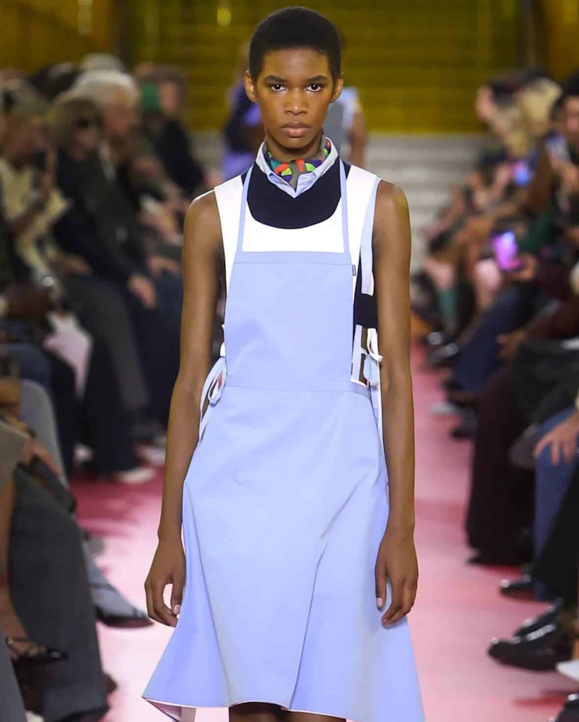 Miu Miu SS26 pale lilac pinafore dress layered over graphic high-neck top.