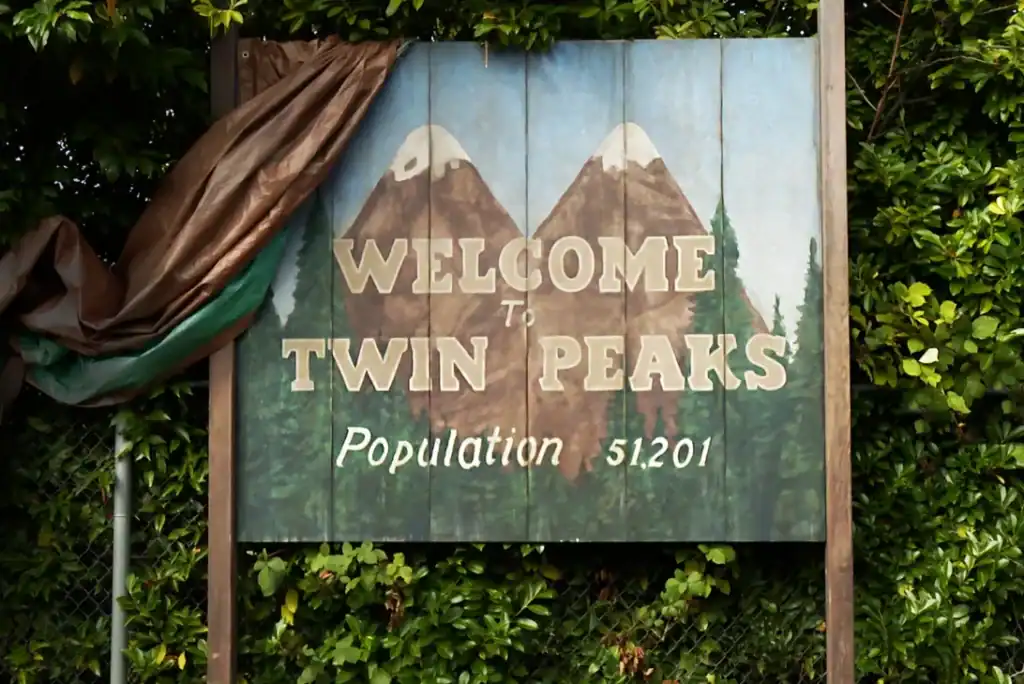 The iconic “Welcome to Twin Peaks” town sign set against a forested backdrop.