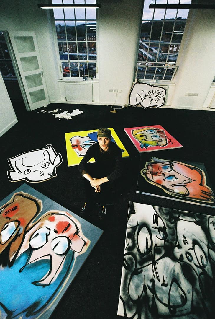 Artist Tomas Gittins sitting in his Manchester studio surrounded by bold, cartoon-like painted canvases