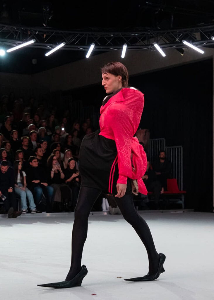 Runway model in a bold pink and black look with exaggerated sculptural shapes by Matil Vanlint
