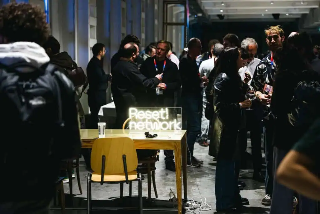 Participants mingling in the Linecheck networking area; in the foreground, a table displays a glowing “Reset! Network” sign.