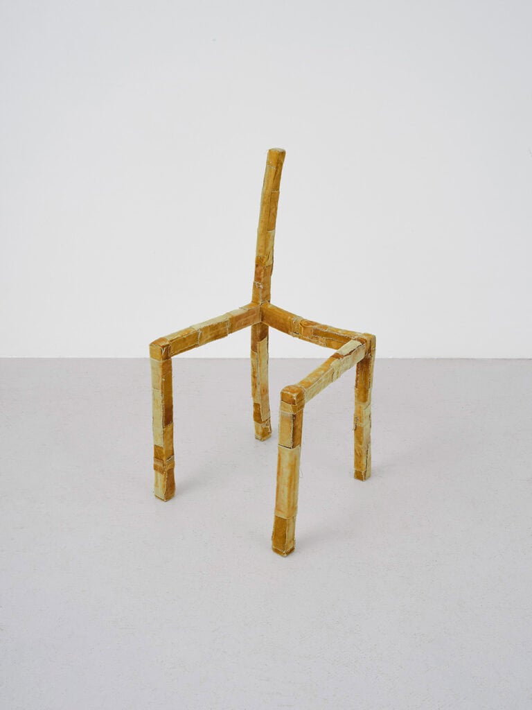 Alice Sheppard Fidler’s sculpture Being Together, a fragile, deconstructed chair form made from taped and wrapped materials, suggesting adaptability, absence, and the traces of human presence.