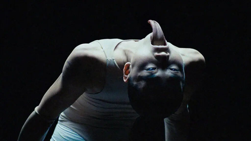 Contortionist dancer in Bonnie Banane’s ‘Hoes of Na’ bending backward in a dark, surreal setting with an elongated tongue effect.