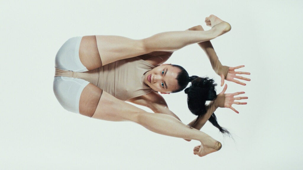 Contortionist performer striking an extreme pose in a minimalist studio for Bonnie Banane’s ‘Hoes of Na’.