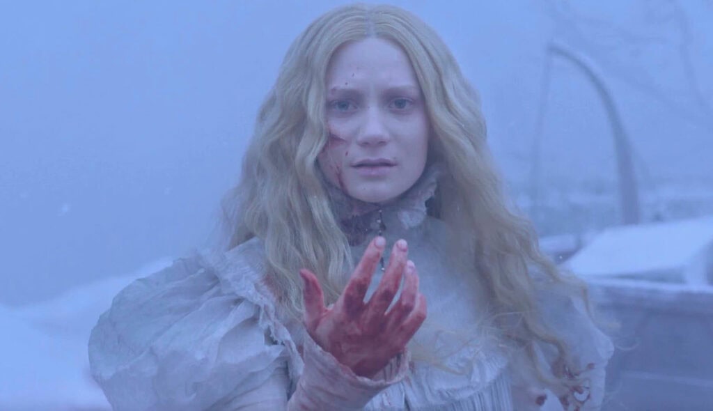 Scene from Crimson Peak showing a woman in a snow-covered landscape holding out a bloodied hand, capturing del Toro’s gothic horror aesthetic