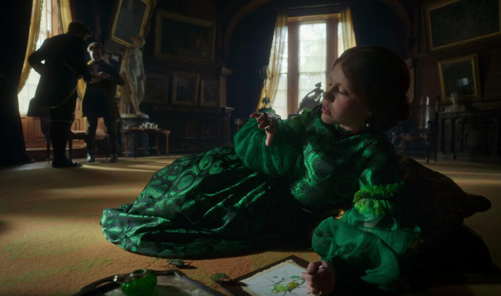 Scene from del Toro’s Frankenstein with a woman in a green Victorian dress sketching in an ornate, shadowy room