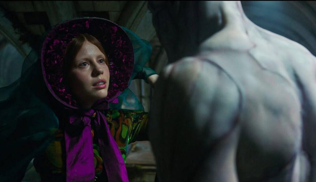 Scene from del Toro’s Frankenstein showing a young woman in a vivid bonnet facing the Creature in a dramatic gothic setting