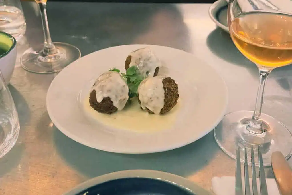 Moussaka-filled croquettes topped with cheese sauce served on a white plate at Vori in London.