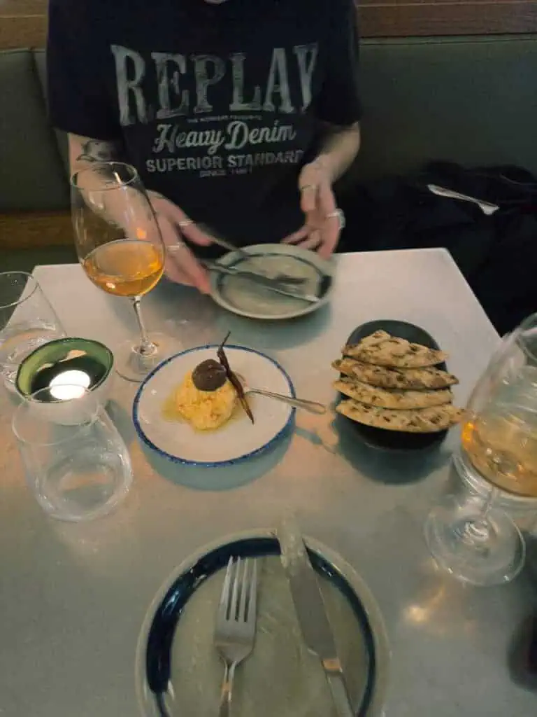 A diner seated at a table at Vori with orange wine, pita, and tirokafteri on the table.