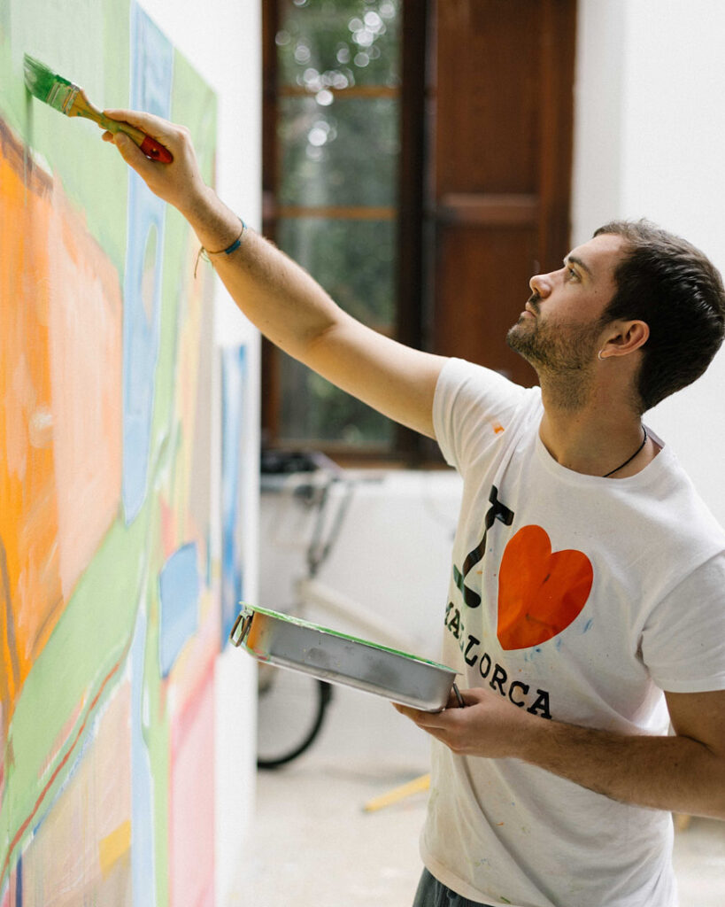 Photograph of Dani Roibal painting a large colourful canvas in his studio, capturing a moment of creative focus.