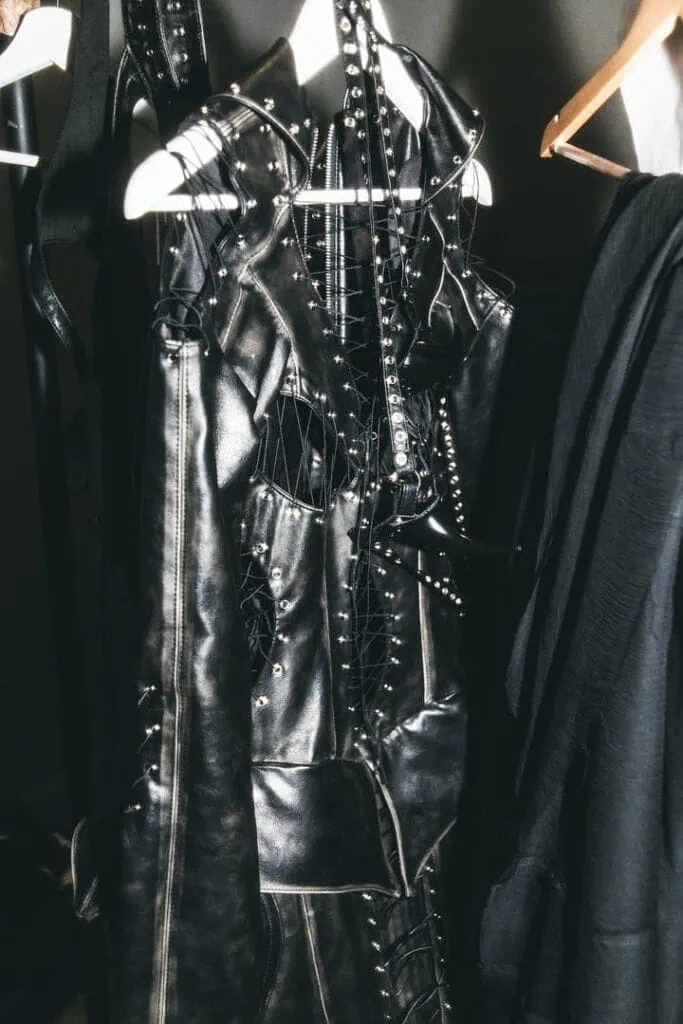JUDASSIME black studded leather garment with lacing and fetish details hanging in backstage.