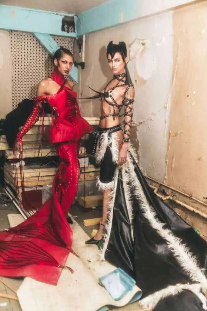 Models in red and black couture looks with sculptural forms and faux fur in distressed backstage.