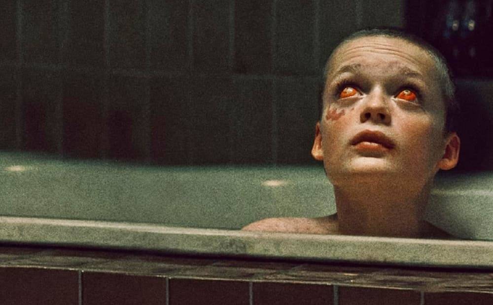 Character with red demonic eyes submerged in bathtub, from Bring her back (2024).