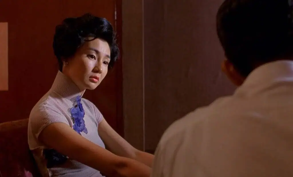 Maggie Cheung’s character sitting in a dimly lit room in “In the Mood for Love,” conveying quiet heartbreak.