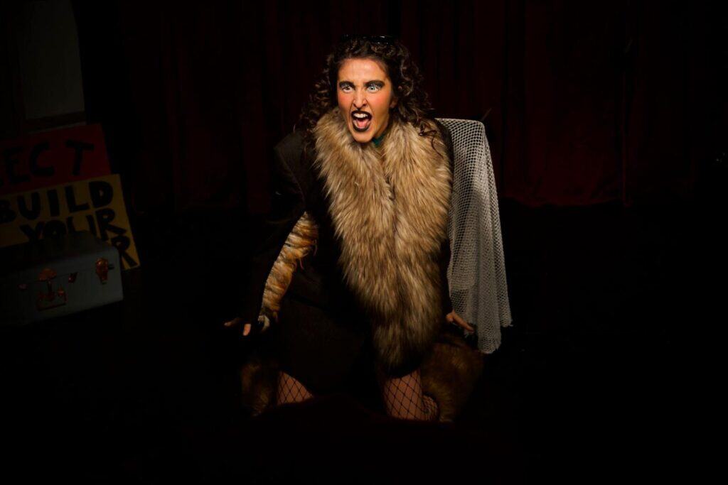 Sofia Natoli in Babel Beast, wearing a fur costume and shouting in a dramatic spotlight.