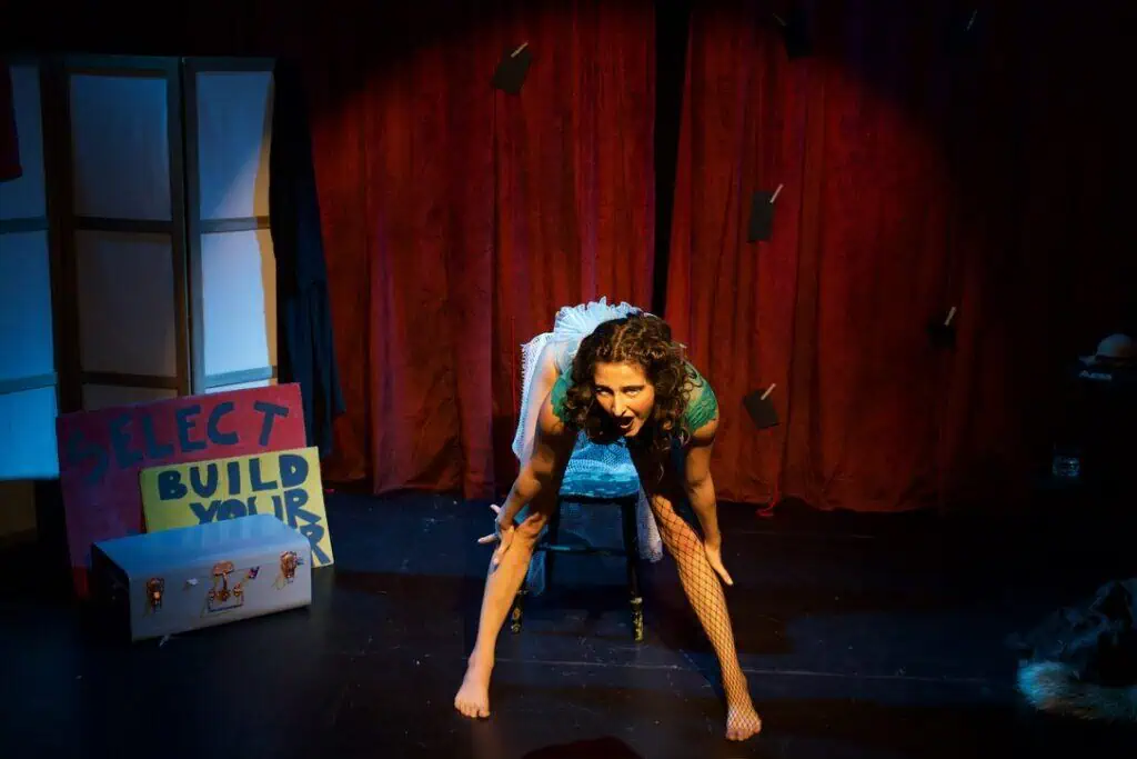 Sofia Natoli on stage in Babel Beast, crouching in a fierce pose before red curtains.