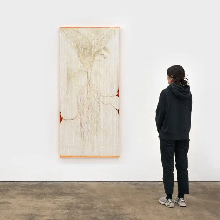 A person in dark clothing stands in a gallery at the Xin-Liu exhibition at Frieze London 2025, viewing a large vertical artwork on a white wall. Abstract, pale lines and shapes resembling roots or branches stretch across a light background.