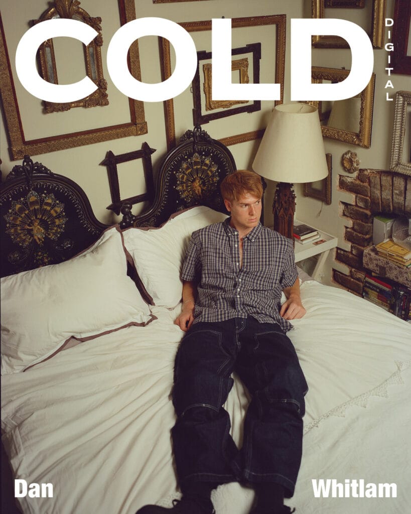 Dan whitlam sits on a white bed in a vintage-style room with framed art and a fireplace. Dan Whitlam’s name appears on the image alongside the words COLD DIGITAL.